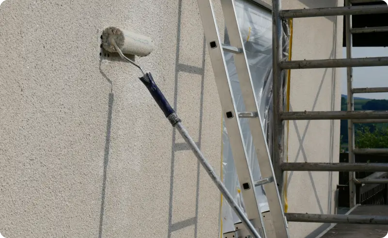 Painting exterior wall with roller and ladder.