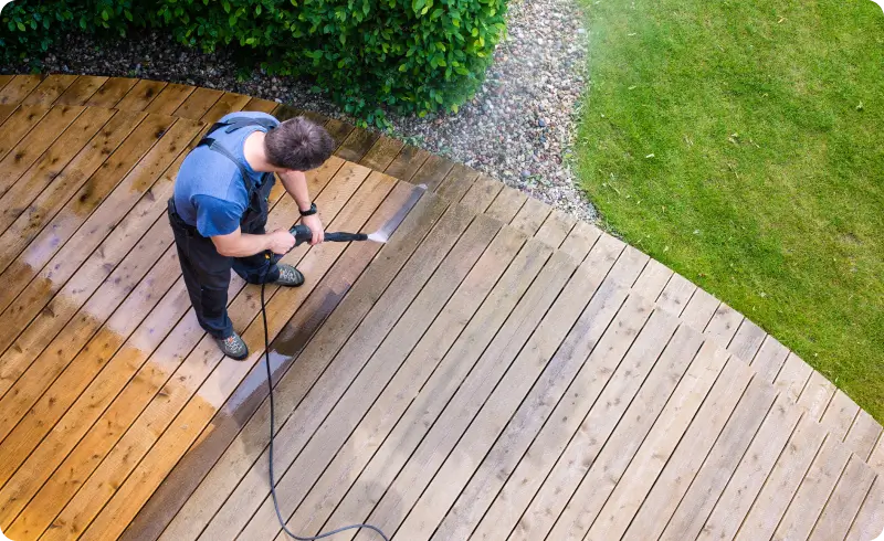 Man pressure washing wooden deck.