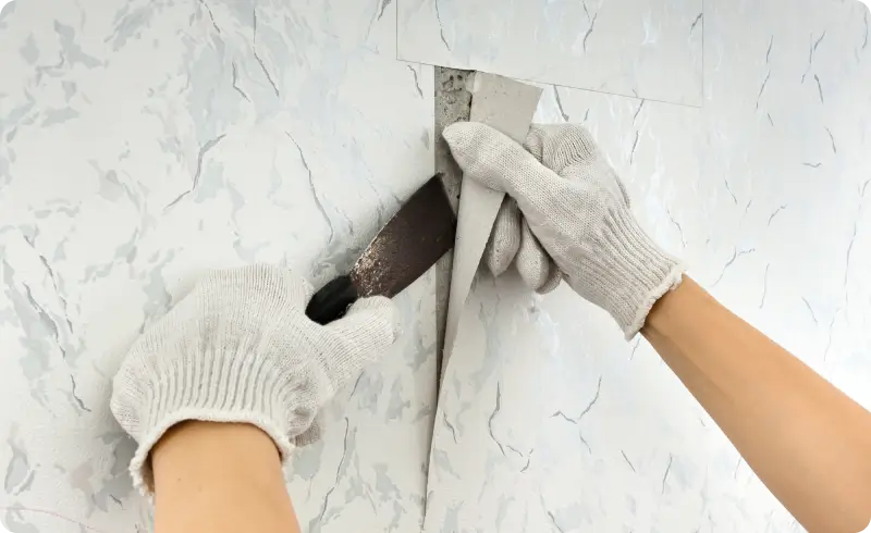 Hands removing wall paneling with tools.