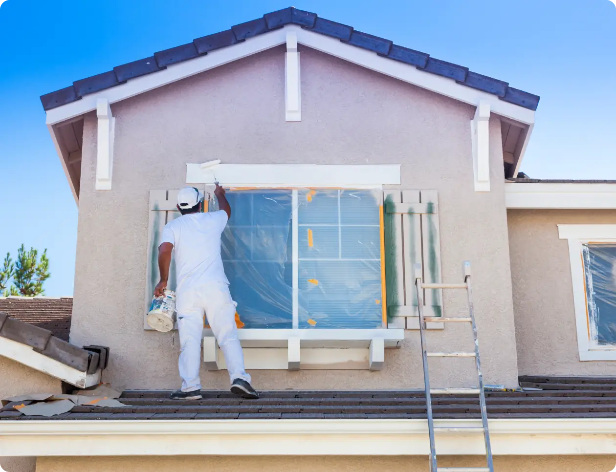 Painter on roof painting house window.