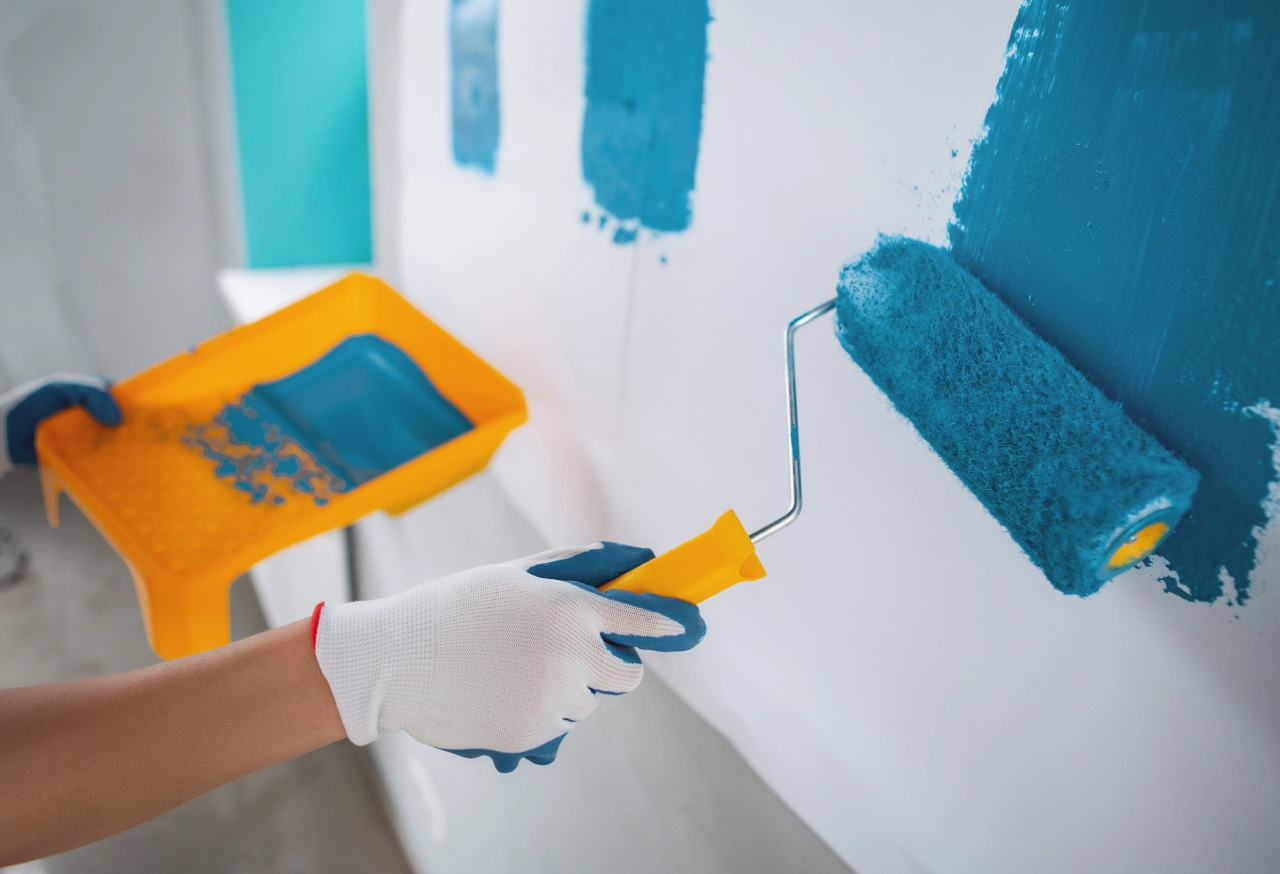 Person painting wall with blue paint roller.