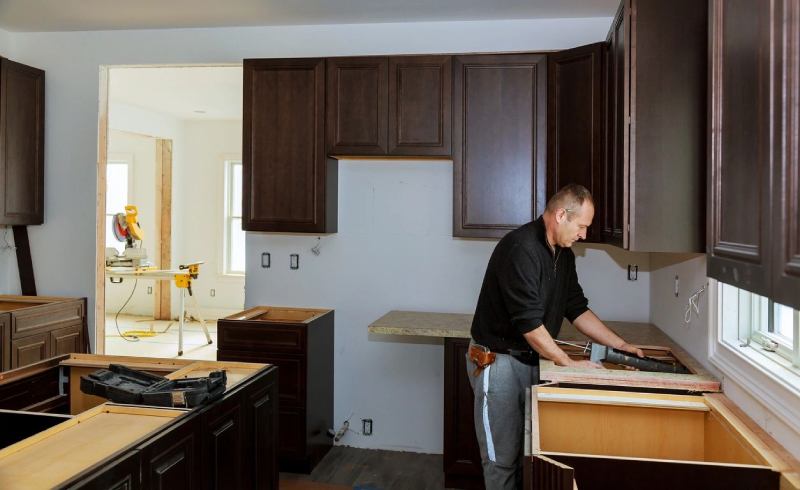 A man in black shirt and gray pants working on a kitchen.